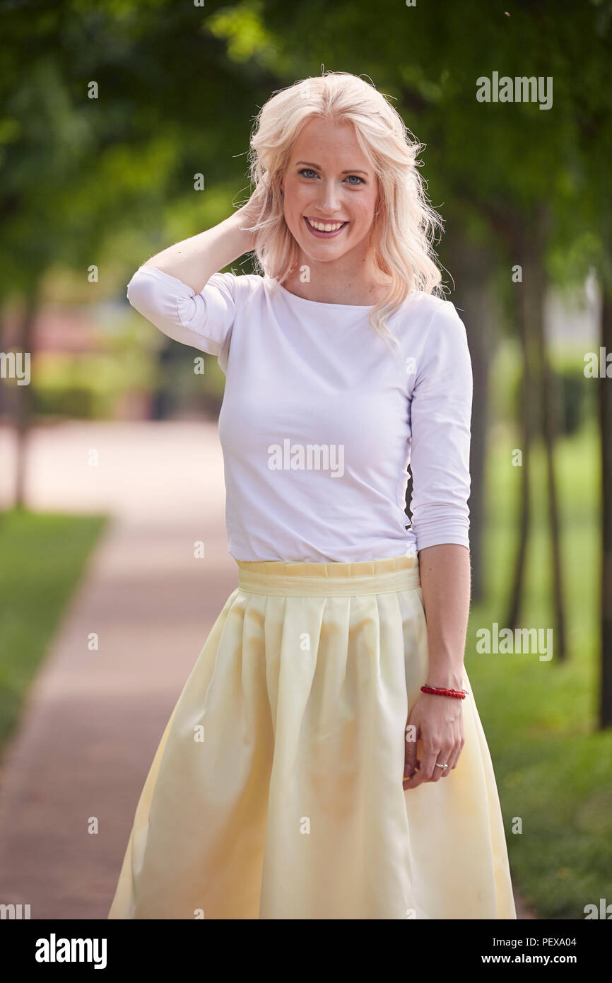 one young woman portrait, 25 years old, yellow dress, white top, park, smiling happy. Stock Photo