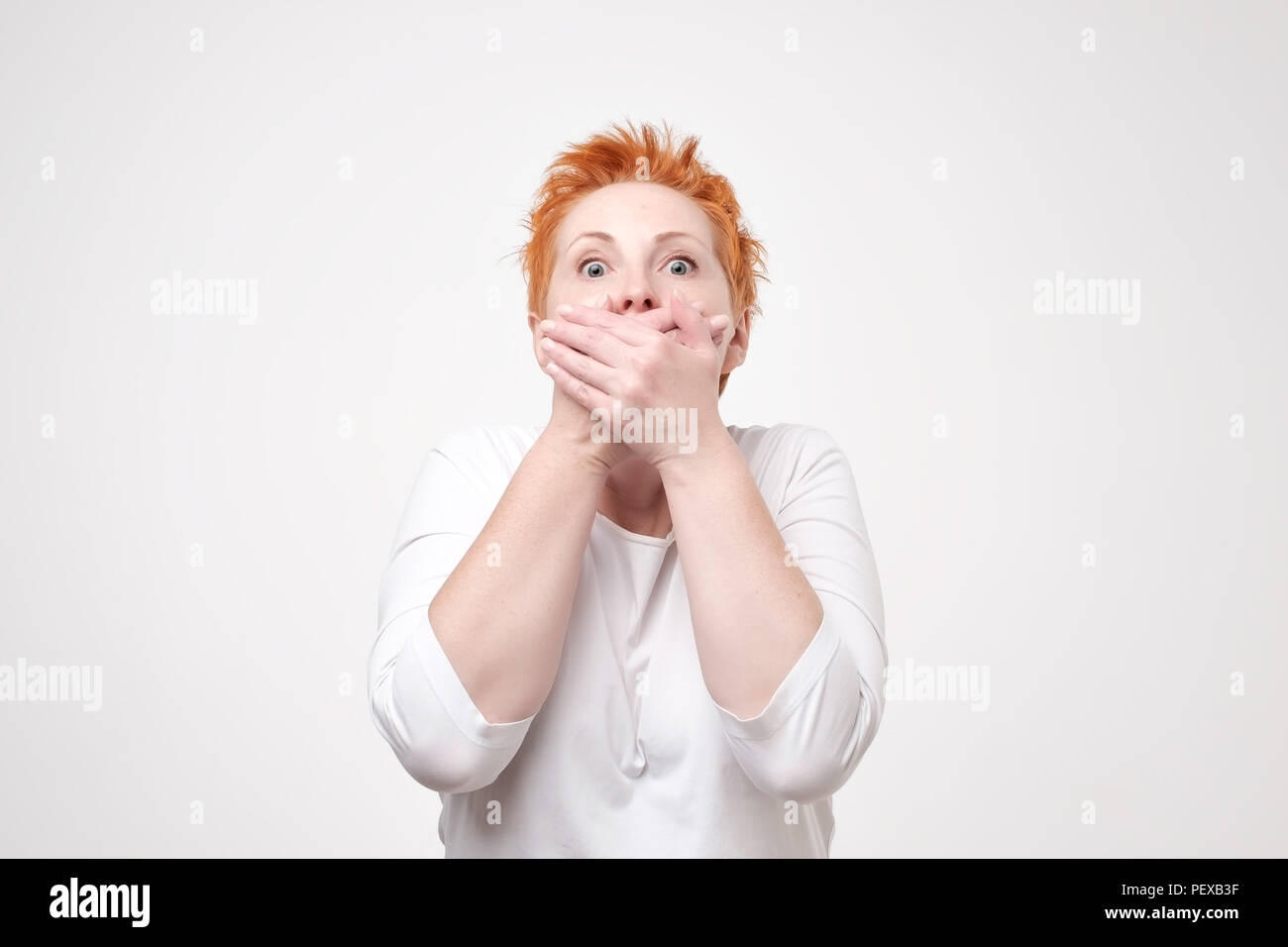 Mature amazed woman covering her mouth with hand on gray background. I wiil not tell this secret anybody. Conspiracy and mystery concept Stock Photo