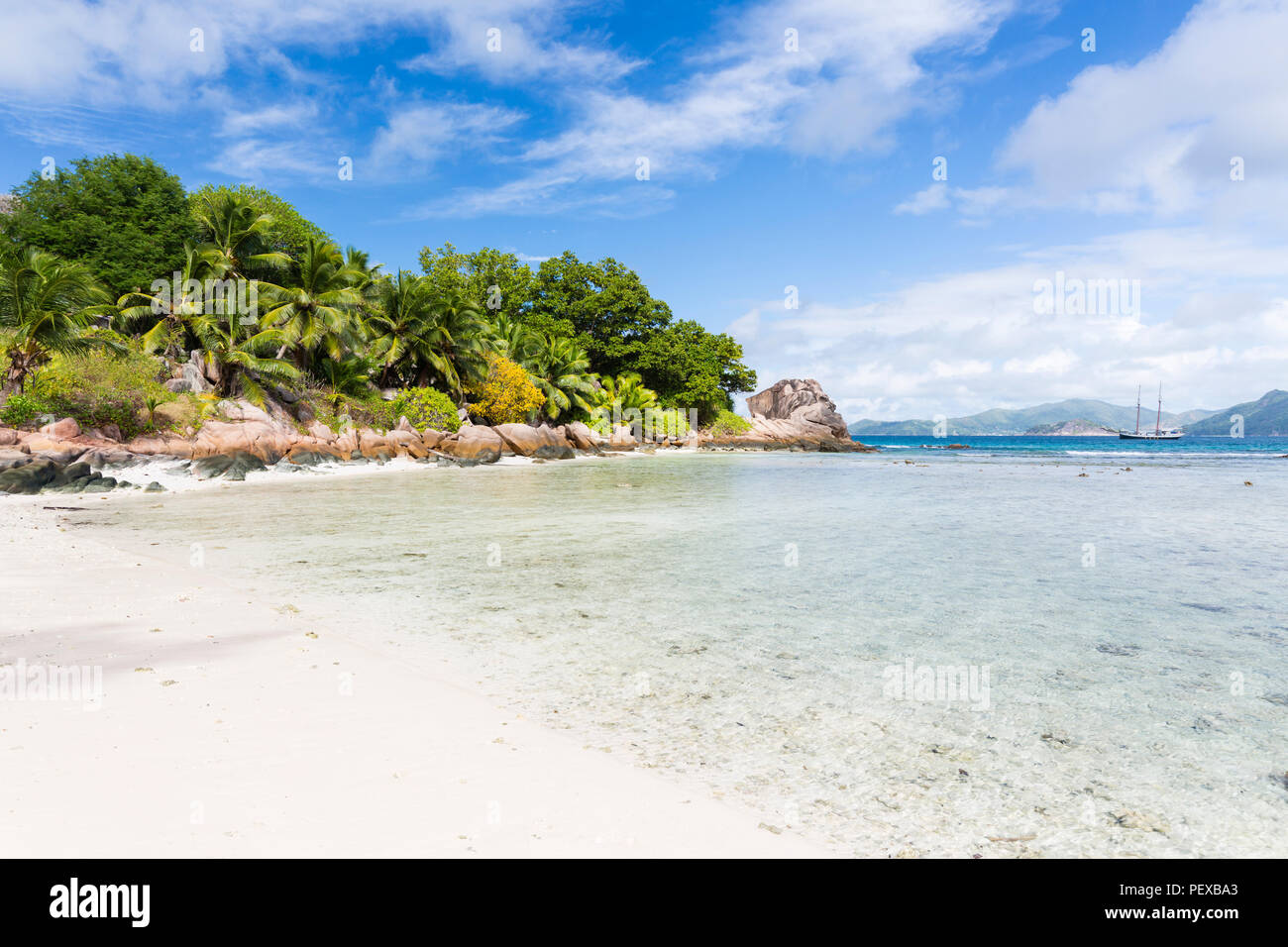 Low tide at Anse Severe in La Digue, Seychelles with some palm trees and granite rocks in the background Stock Photo