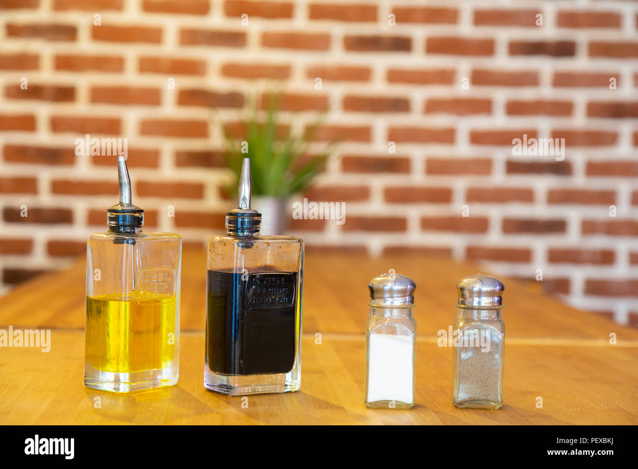 Pepper mill and salt shaker, with bottles of oil and vinegar, on a bamboo table with a brick