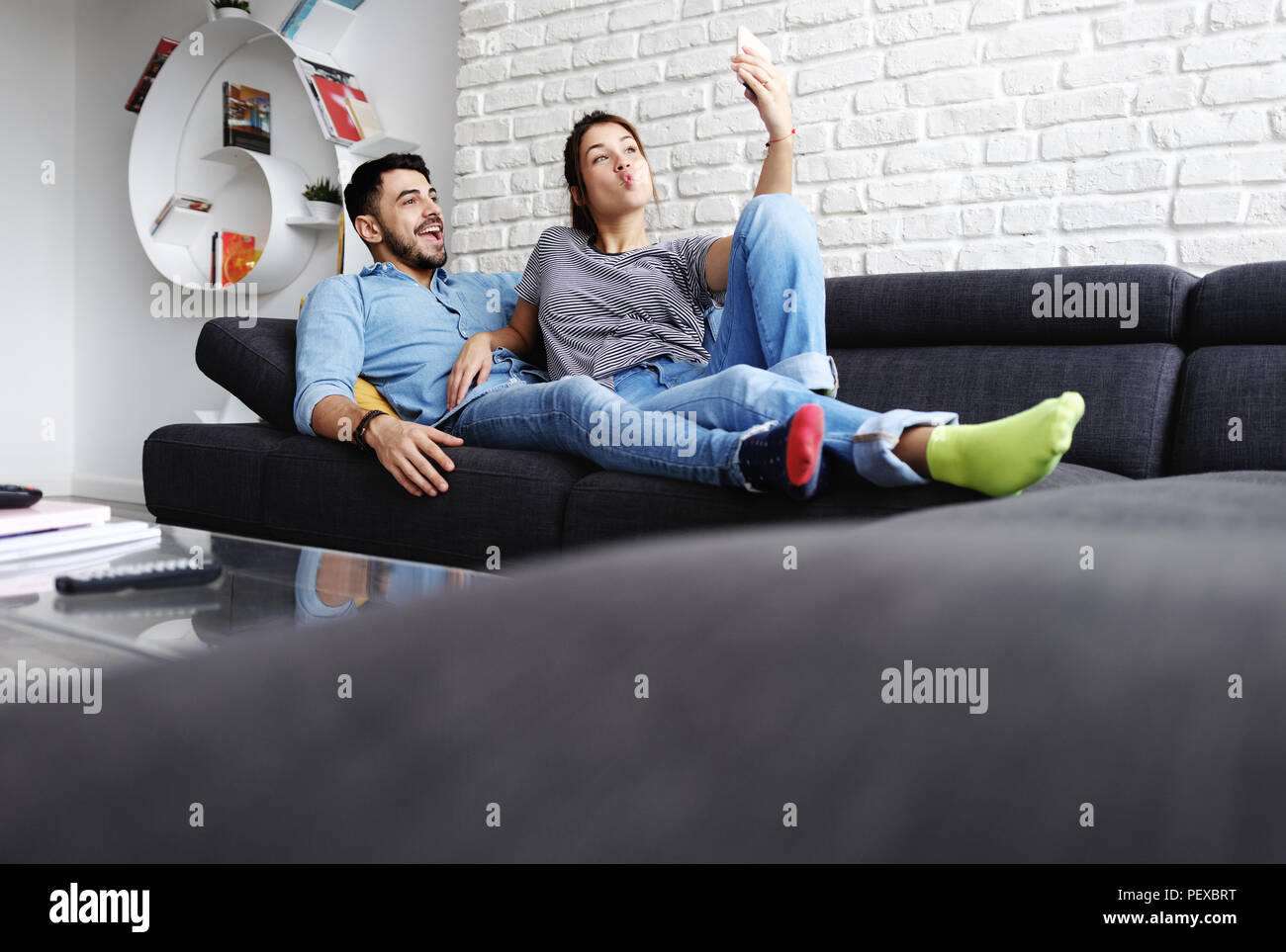 Young Couple Taking Selfie On Sofa At Home Stock Photo