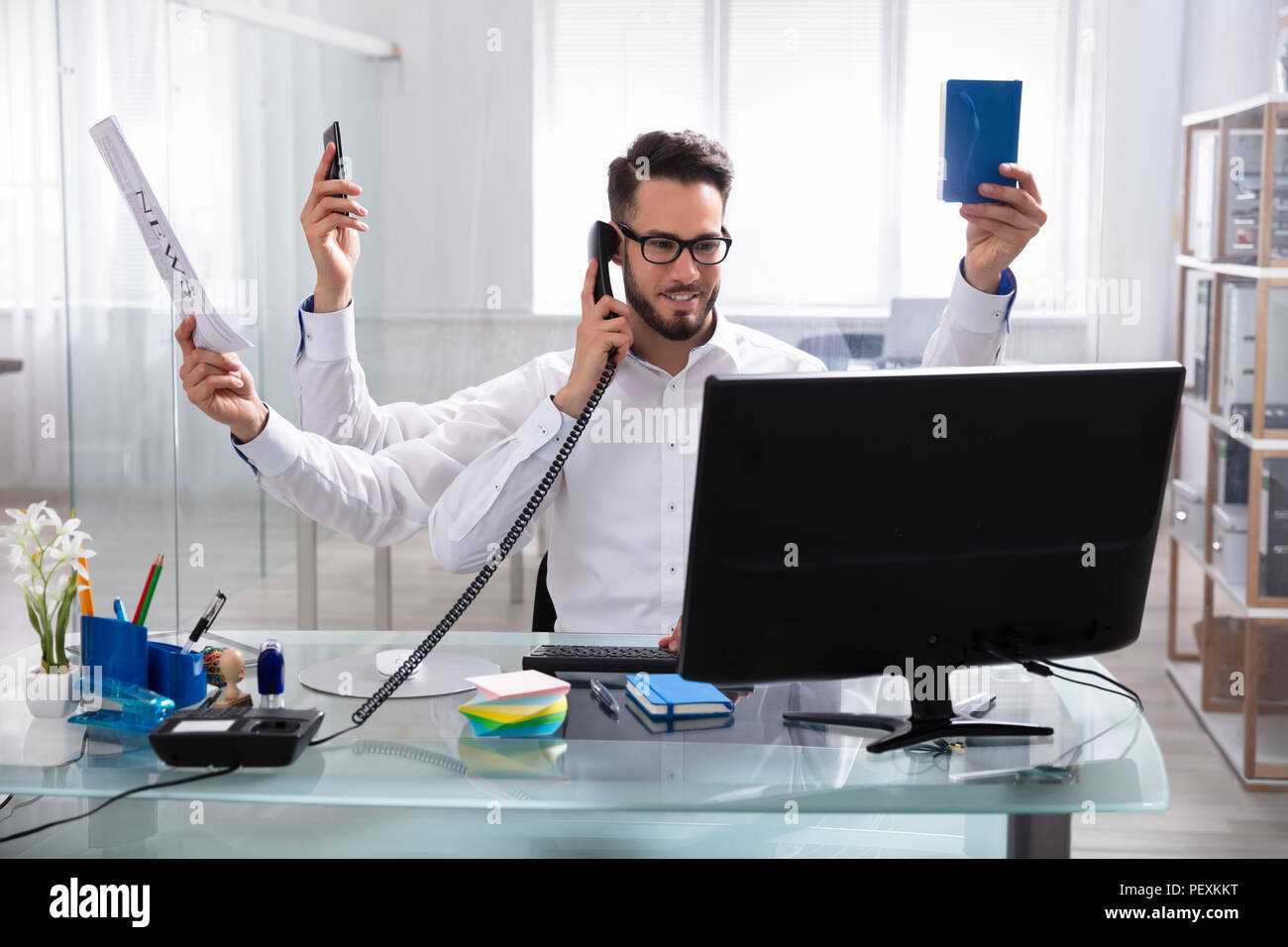 Smiling Young Businessman Doing Multitasking Work At Workplace Stock Photo