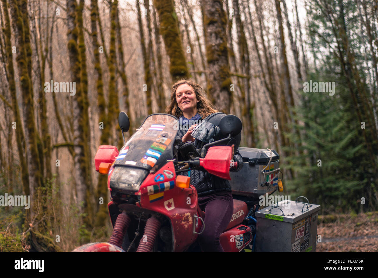 Smiling woman on motorcycle in forest Stock Photo