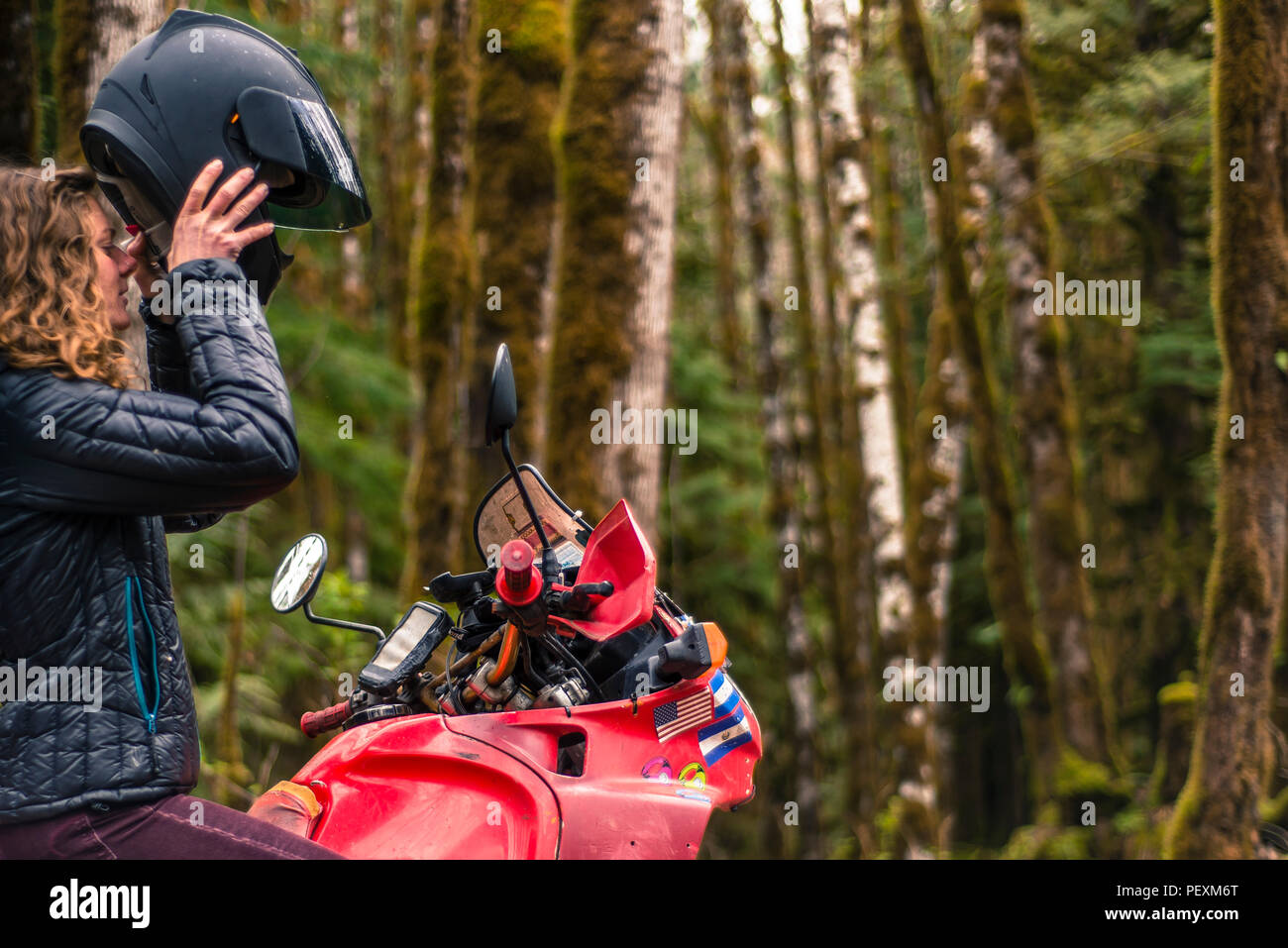Woman on motorcycle taking off crash helmet in forest Stock Photo