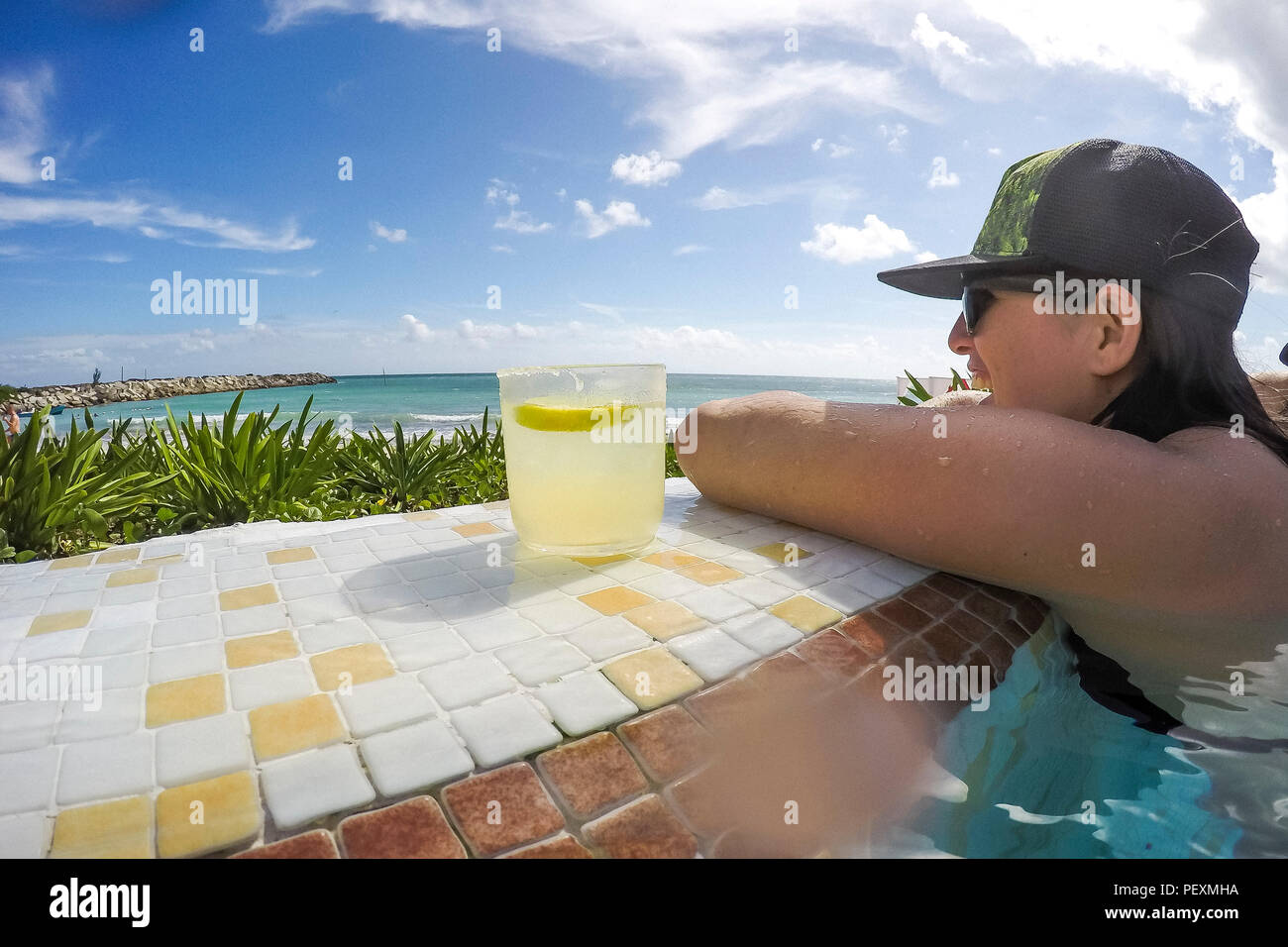 Woman in oceanside swimming pool with cocktail Stock Photo