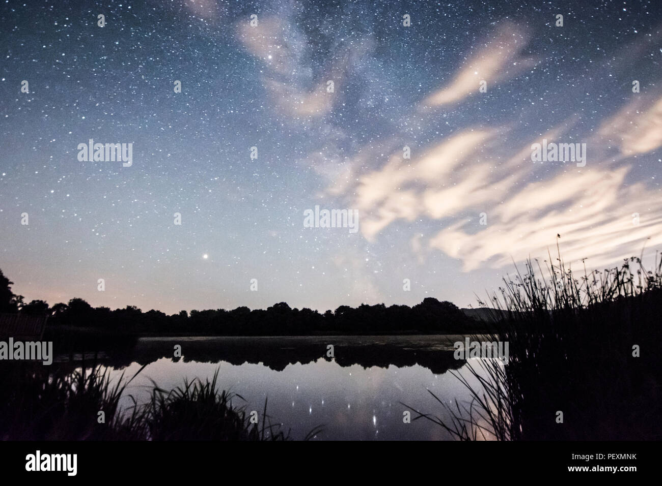 The Milky Way galaxy seen over Burton Mill Pond, thin wispy clouds, The South Downs National Park, Petworth, Sussex, UK. August. Night. Stock Photo