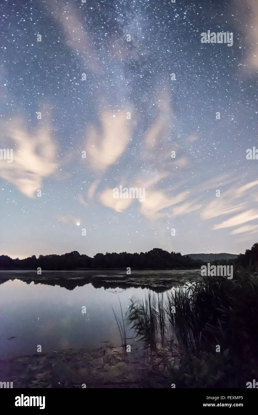 The Milky Way galaxy seen over Burton Mill Pond, thin wispy clouds, The South Downs National Park, Petworth, Sussex, UK. August. Night. Stock Photo