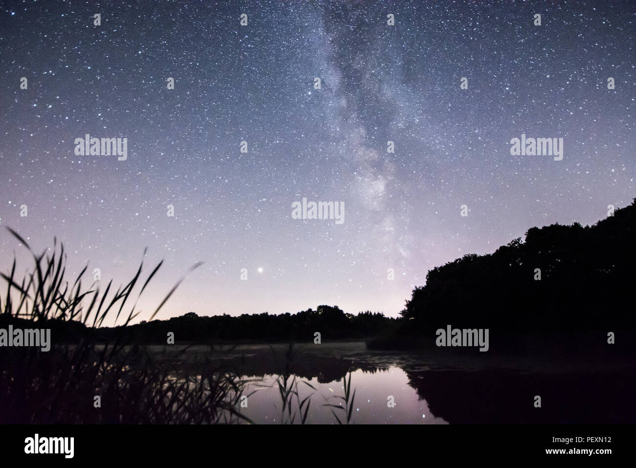 The Milky Way galaxy seen over Burton Mill Pond, The South Downs National Park, Petworth, Sussex, UK. August. Night. Stock Photo