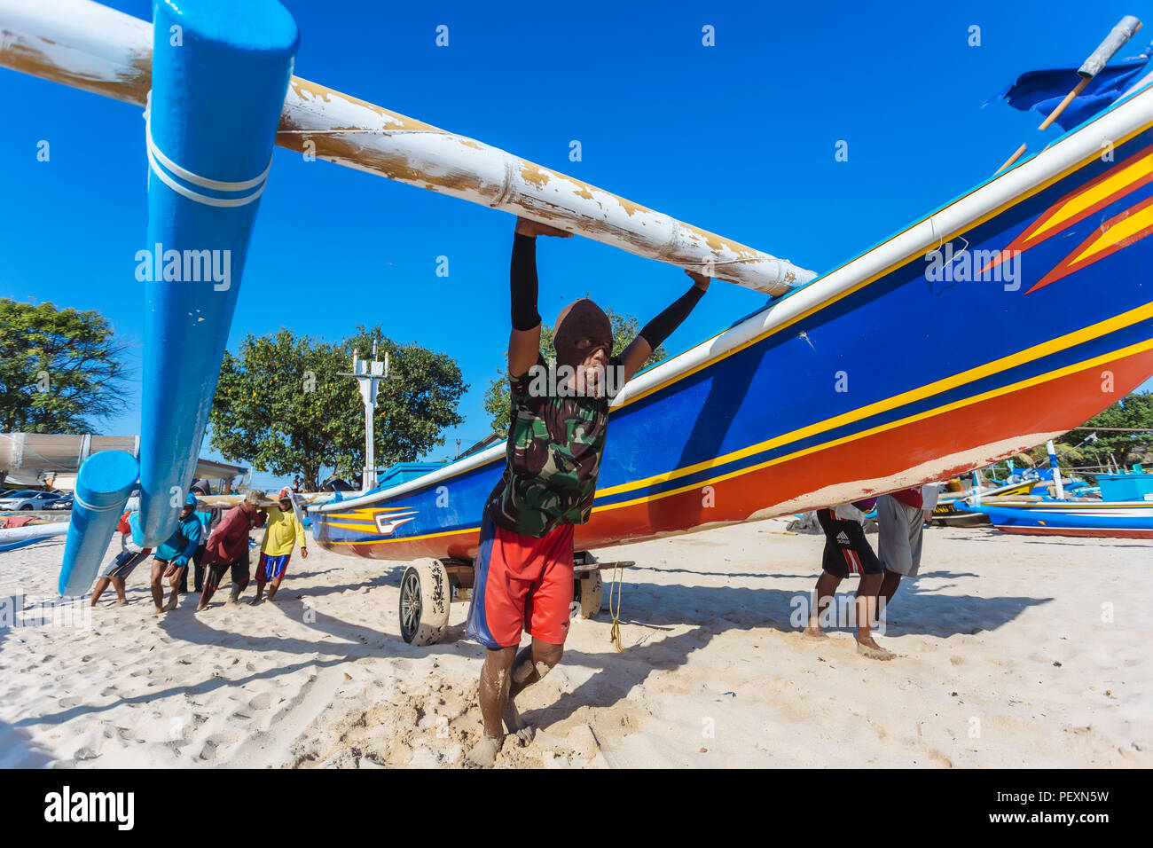 Men pushing boat on beach, Jimbaran, Bali, Indonesia Stock Photo