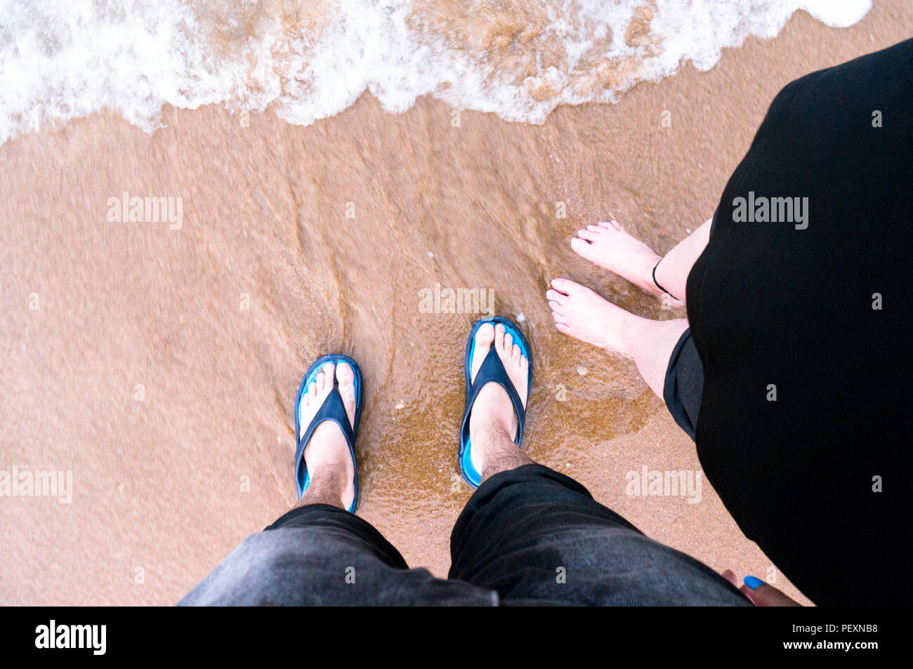 downward looking shot of couple standing on a beach with waves c Stock Photo
