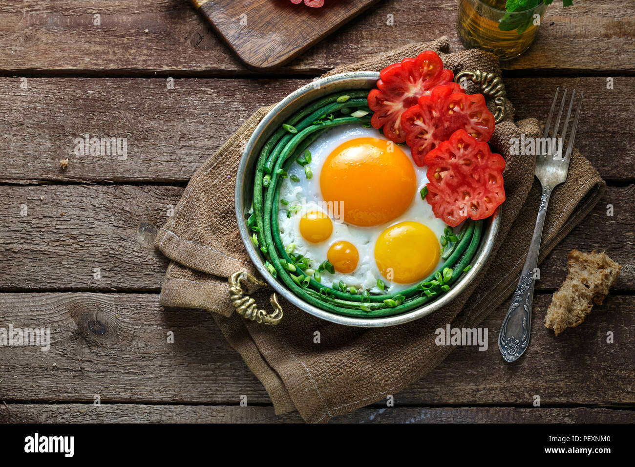 Sunny side fried eggs in a copper pan with tomatoes and green beans