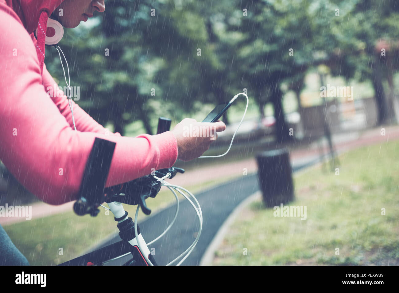 Close up of man on bike in a park, while looking at mobile phone. Rainy day. Stock Photo