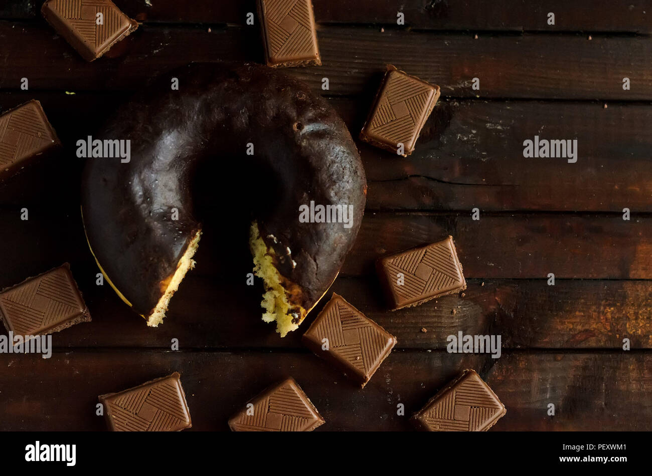 Bitten chocolate donut with coffee and milk chocolate on wooden background.Sweet dessert in the morning.Copyspace right. Stock Photo