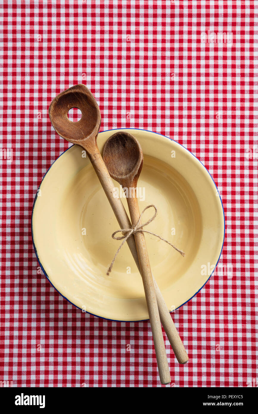 Rustic place setting. Empty plate, wooden kitchen utensils and red tablecloth, top view Stock Photo