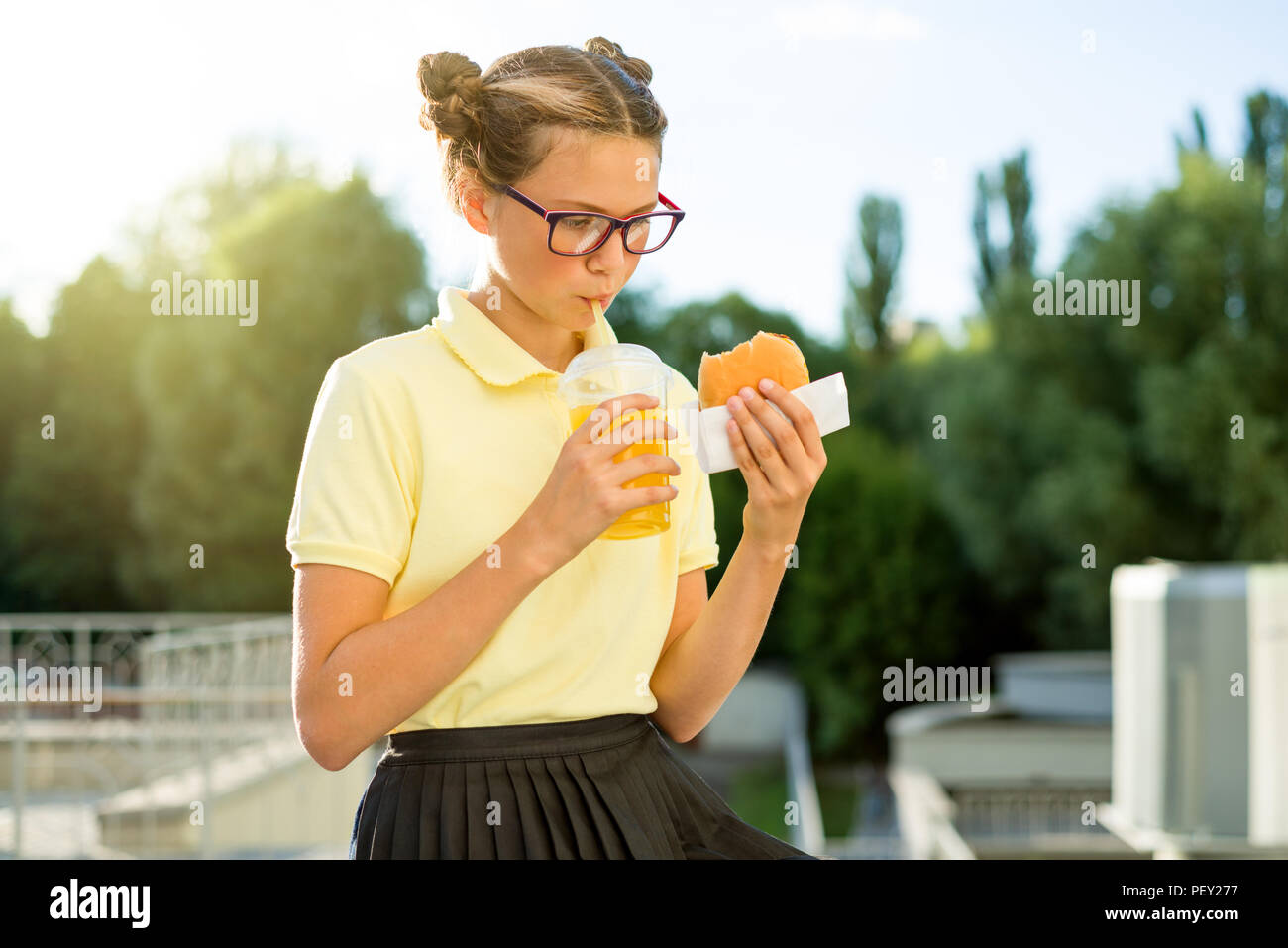 Cute smiling schoolgirl teenager holding a hamburger and orange juice. Back to school outdoor Stock Photo
