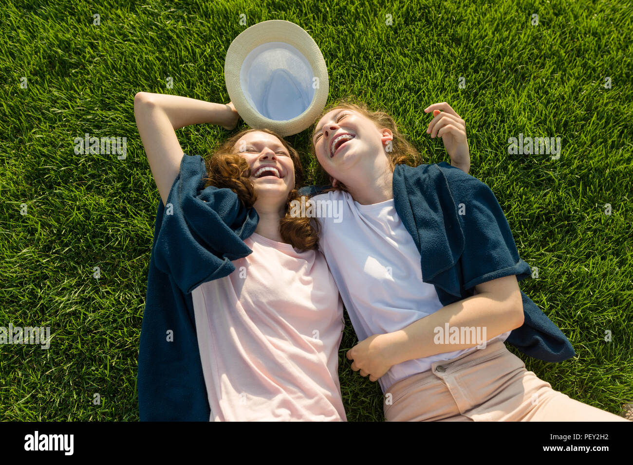 Girls teenagers having fun, lie on the green grass, laughing, top view Stock Photo