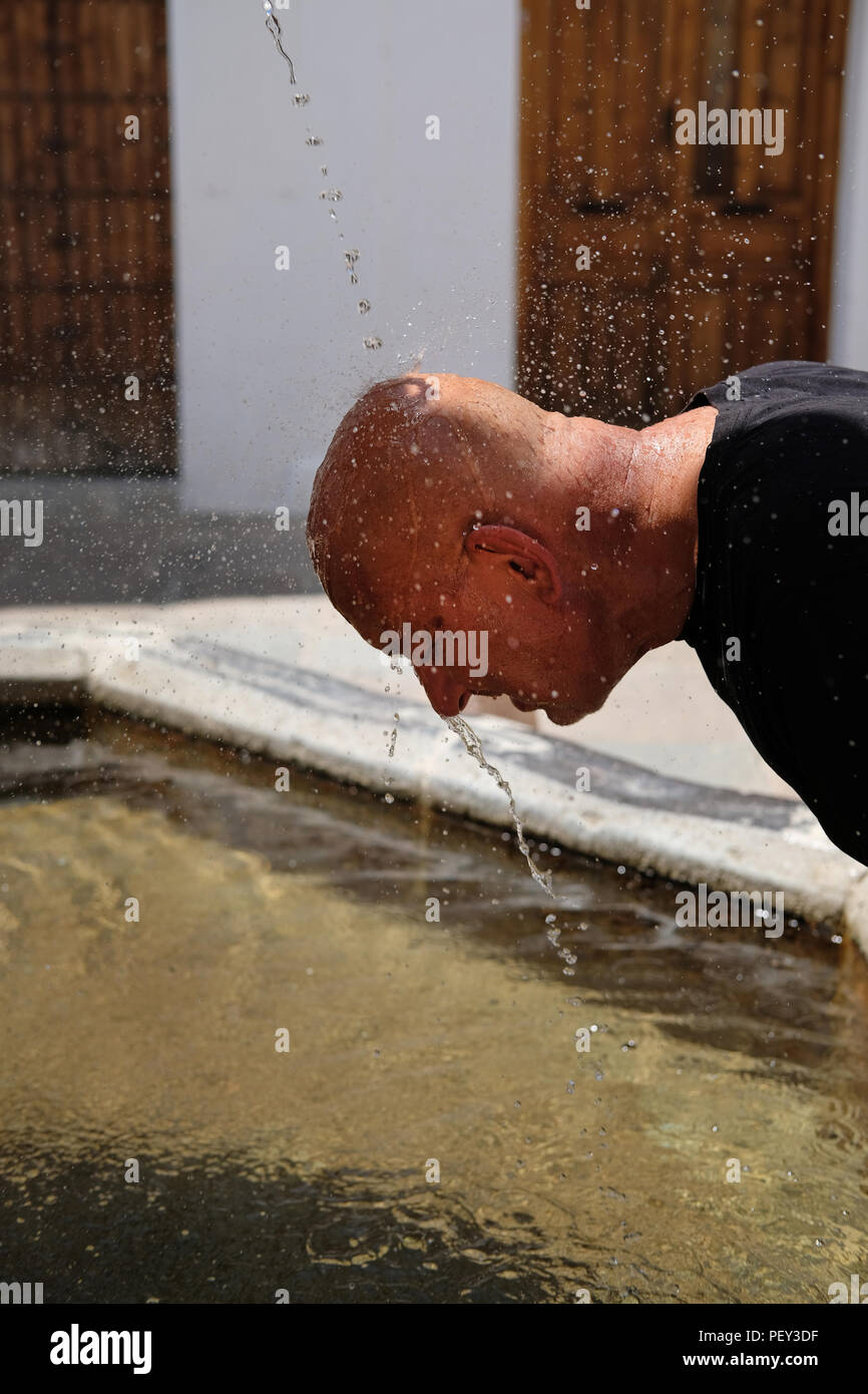 A tourist in Spain cools down at a water fountain. Stock Photo
