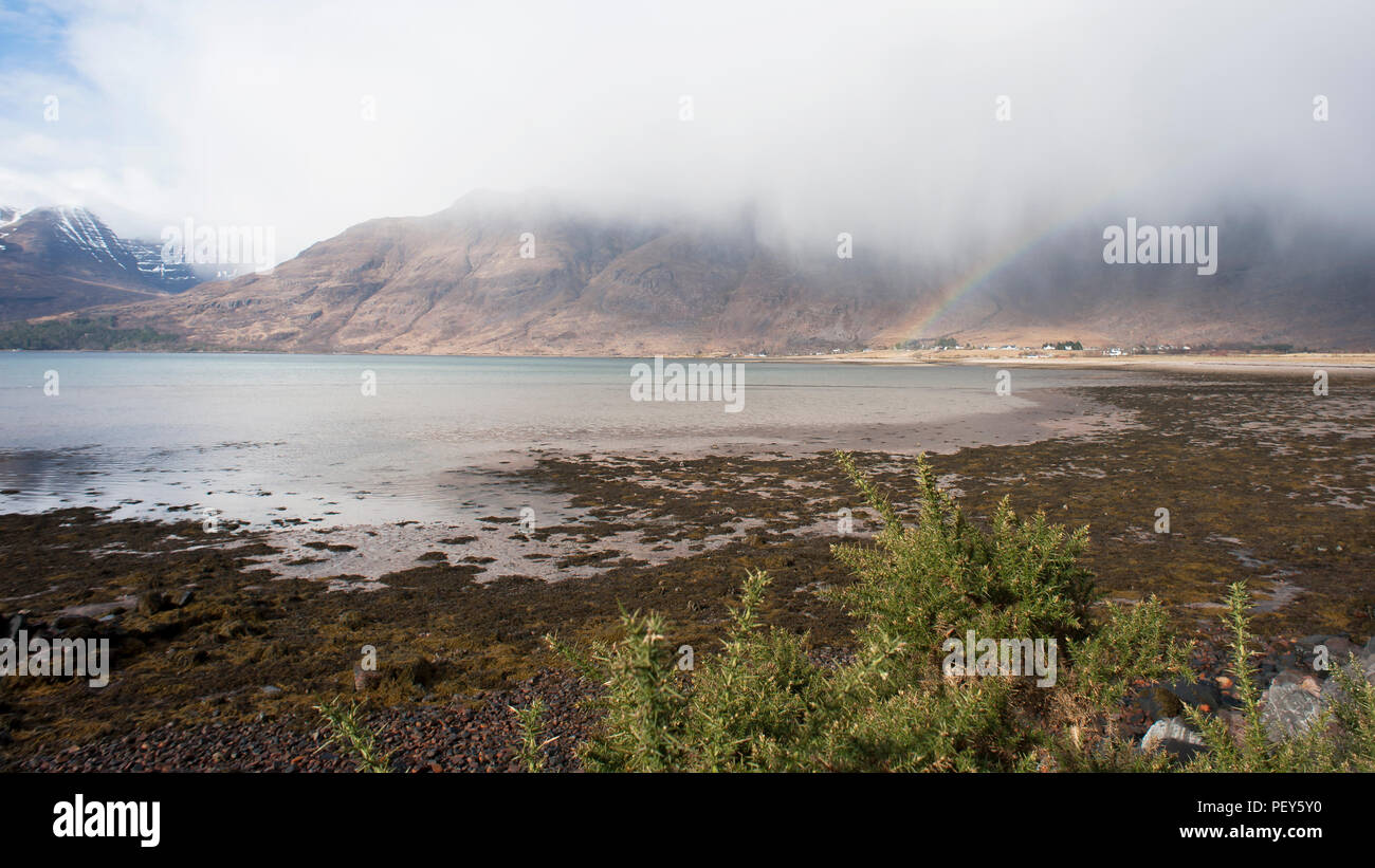 View over Loch Torridon of rainbow underneath low rain cloud arching over Torridon Village in the Highlands of Scotland Stock Photo