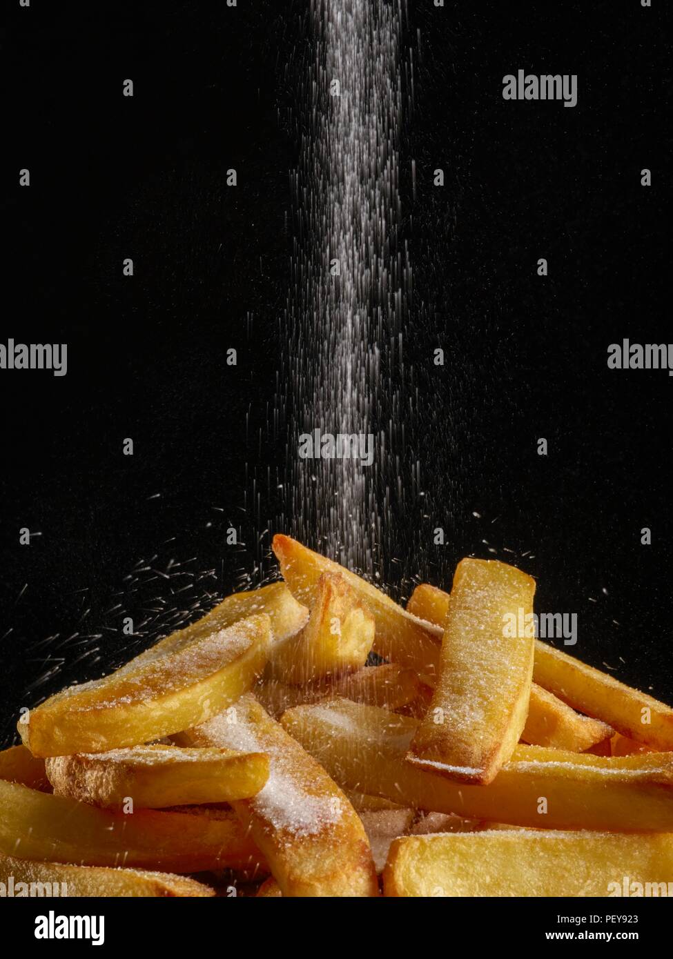 Salt pouring onto chips. Stock Photo