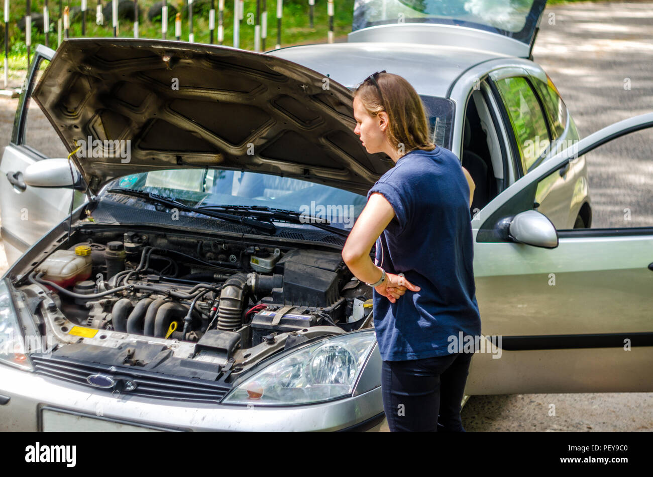 Girl driver near the open hood of a broken car. Broken car on the