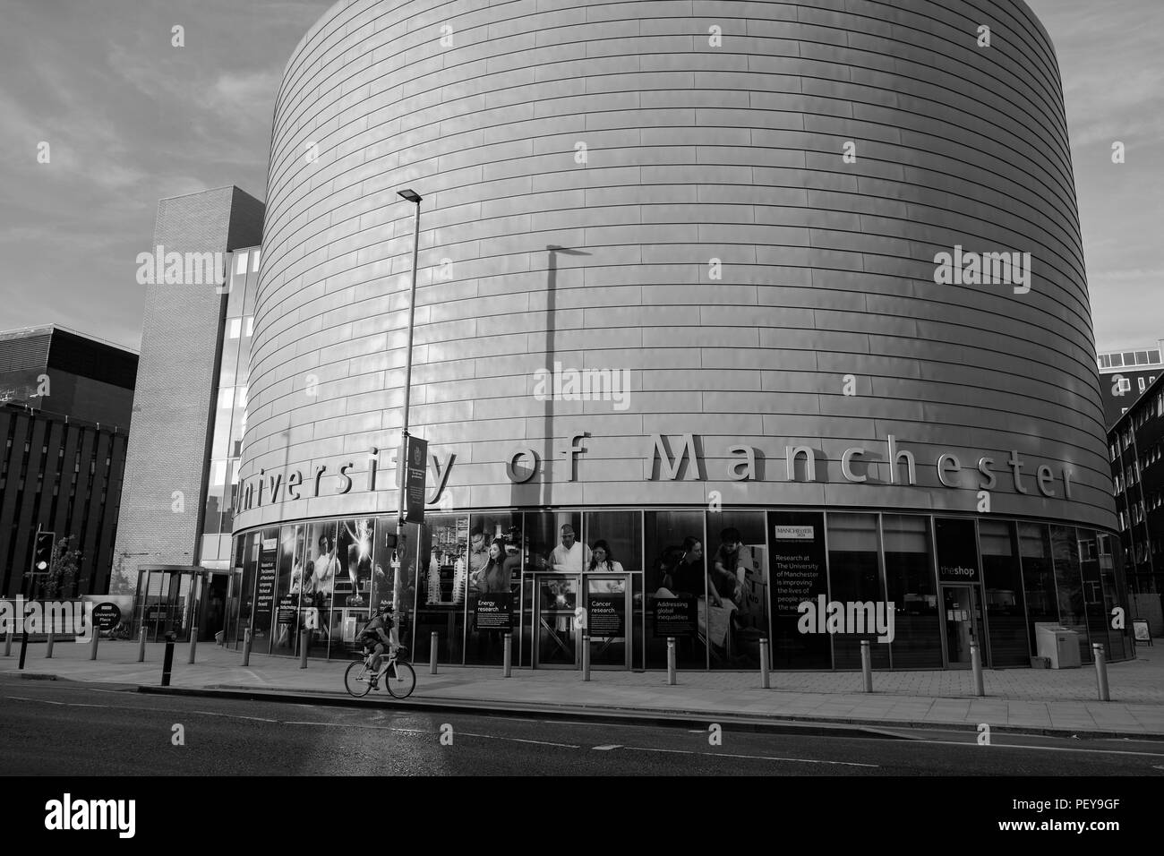 Manchester, United Kingdom - July 25, 2018: A cyclist passes by the large, drum-shaped building of The University of Manchester, University Place Stock Photo