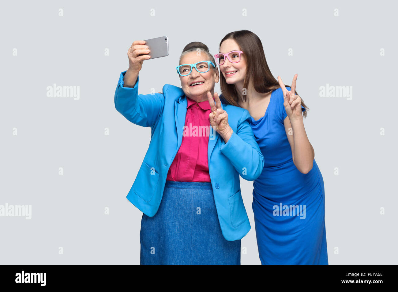 happy grandmother with granddaughter in blue dress or suit toothy smiling, standing, posing and making selfie and peace sign. Relations in the family. Stock Photo