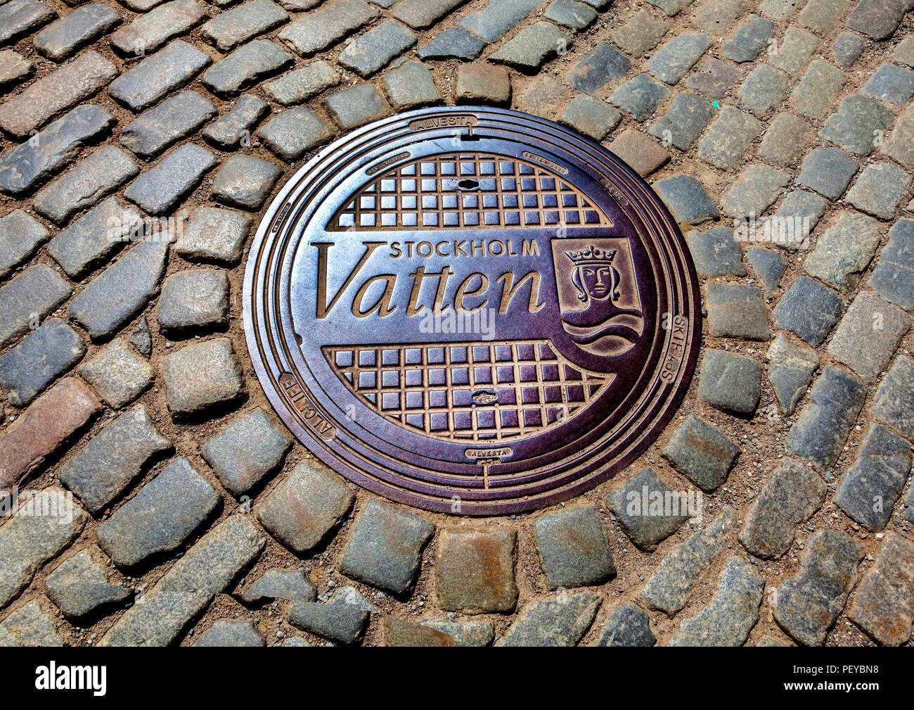 Manhole cover in cobbled street in the Old Town area of Stockholm. Stockholm Vatten AB is a water and waste management company in Sweden. Stock Photo