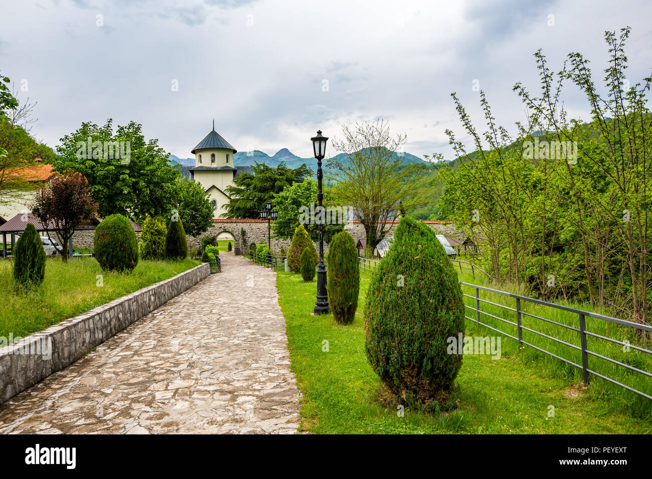 Stone patio in park with green spring grass, bushes and trees leading to the yard of beautiful Orthodox church in Serbia Stock Photo