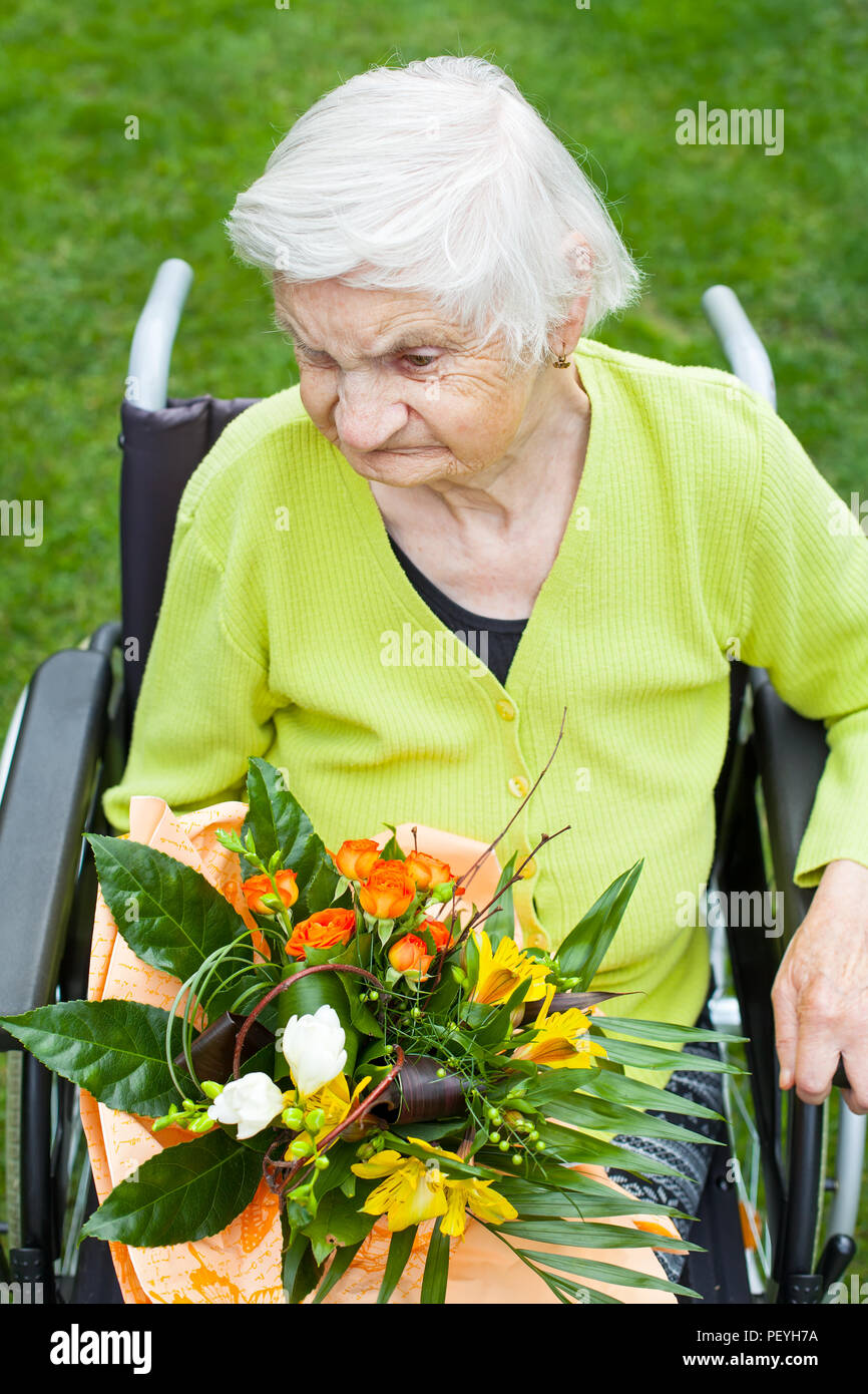 Disabled elderly woman sitting in wheelchair, receiving a flower