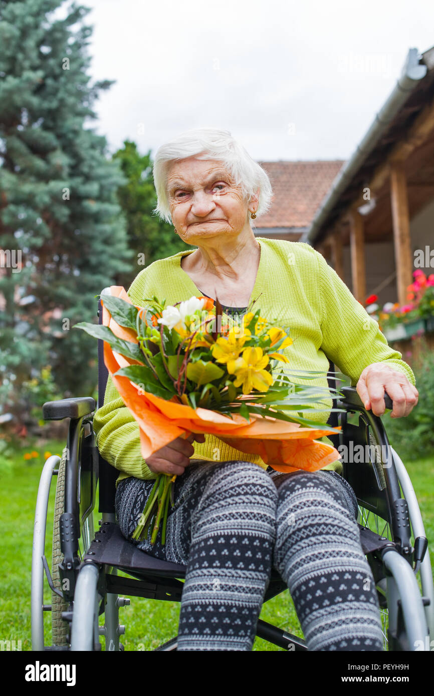 Disabled elderly woman sitting in wheelchair, receiving a flower