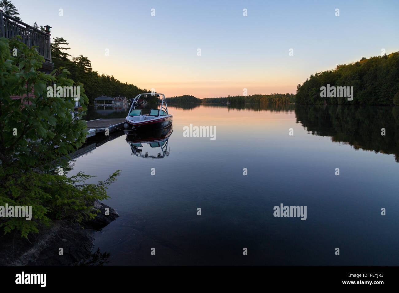 A boathouse with a wakeboard boat parked at it on Lake Joseph at dawn. Stock Photo