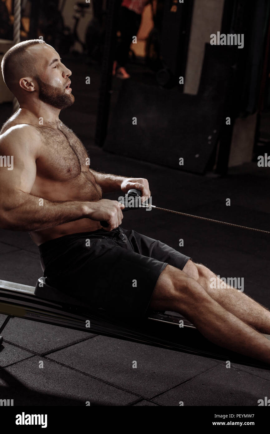 a tired sporty man sitting on the indoor rower at gym. people and fitness concept Stock Photo