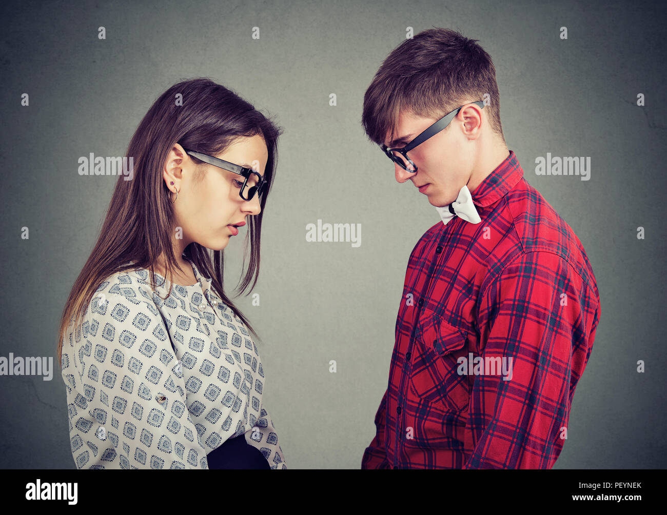 Side view of young man and woman looking down standing opposite with feelings of regret and sadness Stock Photo