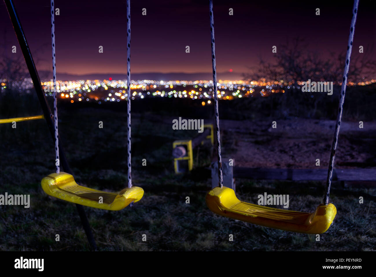 Empty swings on the night with city lights blurred on the background in a winter night Stock Photo