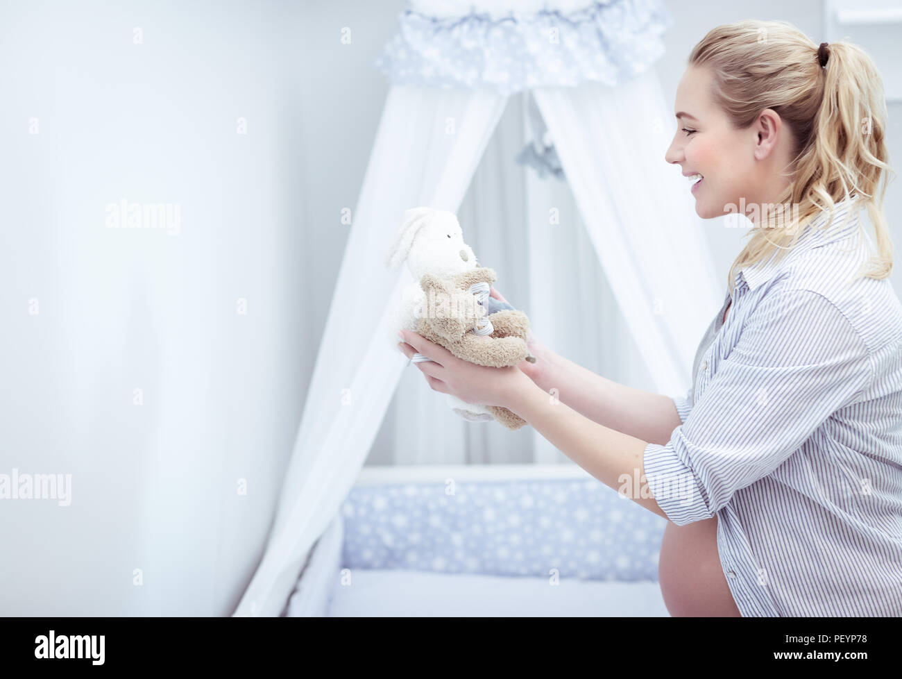 Happy mother prepares child's room, beautiful young pregnant woman with pleasure decorates bed of her future baby with toys, happy pregnancy concept Stock Photo