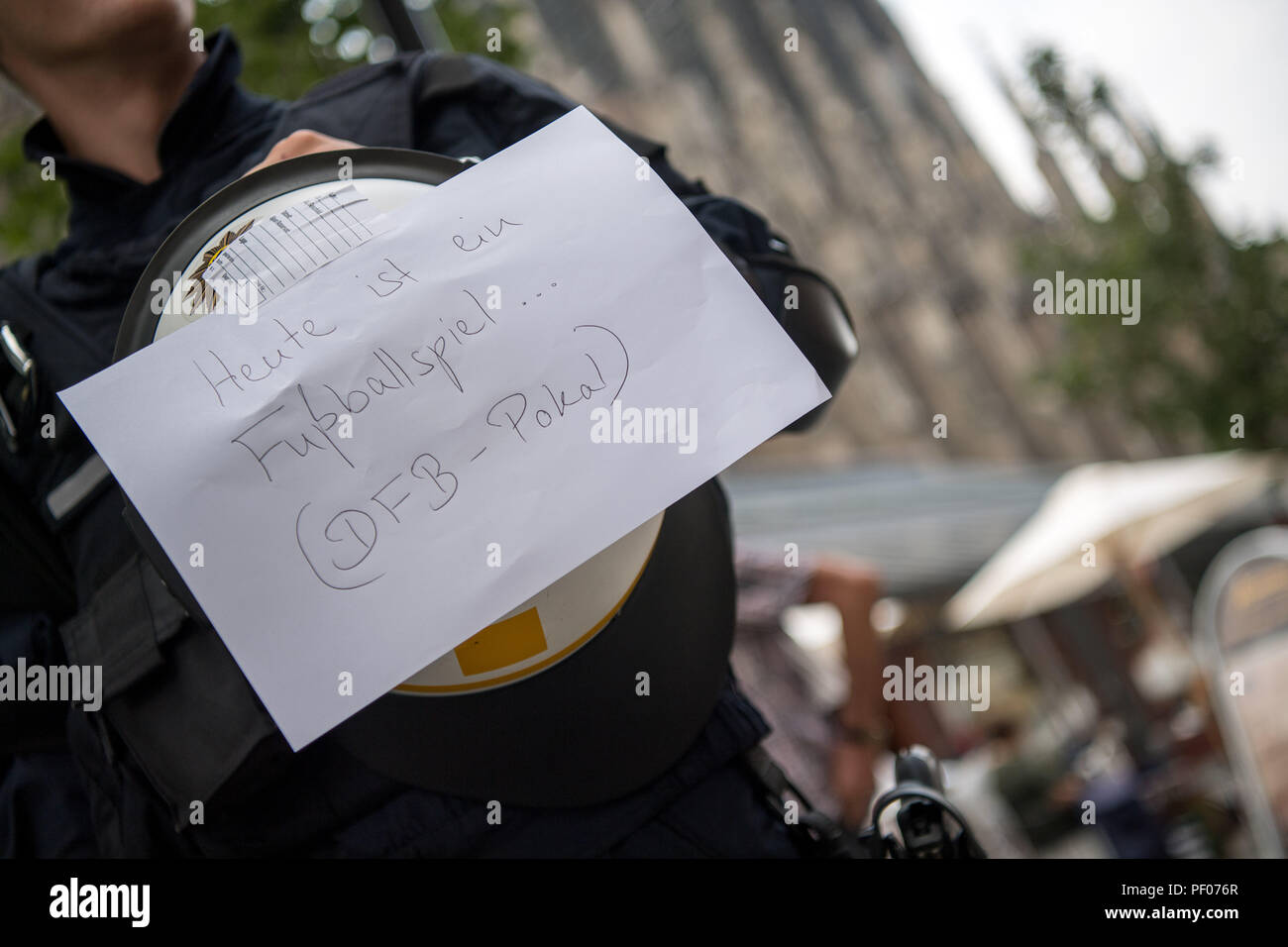 Ulm, Germany. 18th Aug, 2018. A note reading 'Heute ist ein Fussballspiel. (DFB Pokal)' (lit. 'Today is a football mathc.DFB Trophy) is attached to the helmet of a police officer before a football match of the DFB Cup SSV Ulm 1846 against Eintracht Frankfurt. The note is a reaction to the many inquiries from citizens of Ulm as to why so many police are on the move in the city. Credit: Sebastian Gollnow/dpa/Alamy Live News Stock Photo