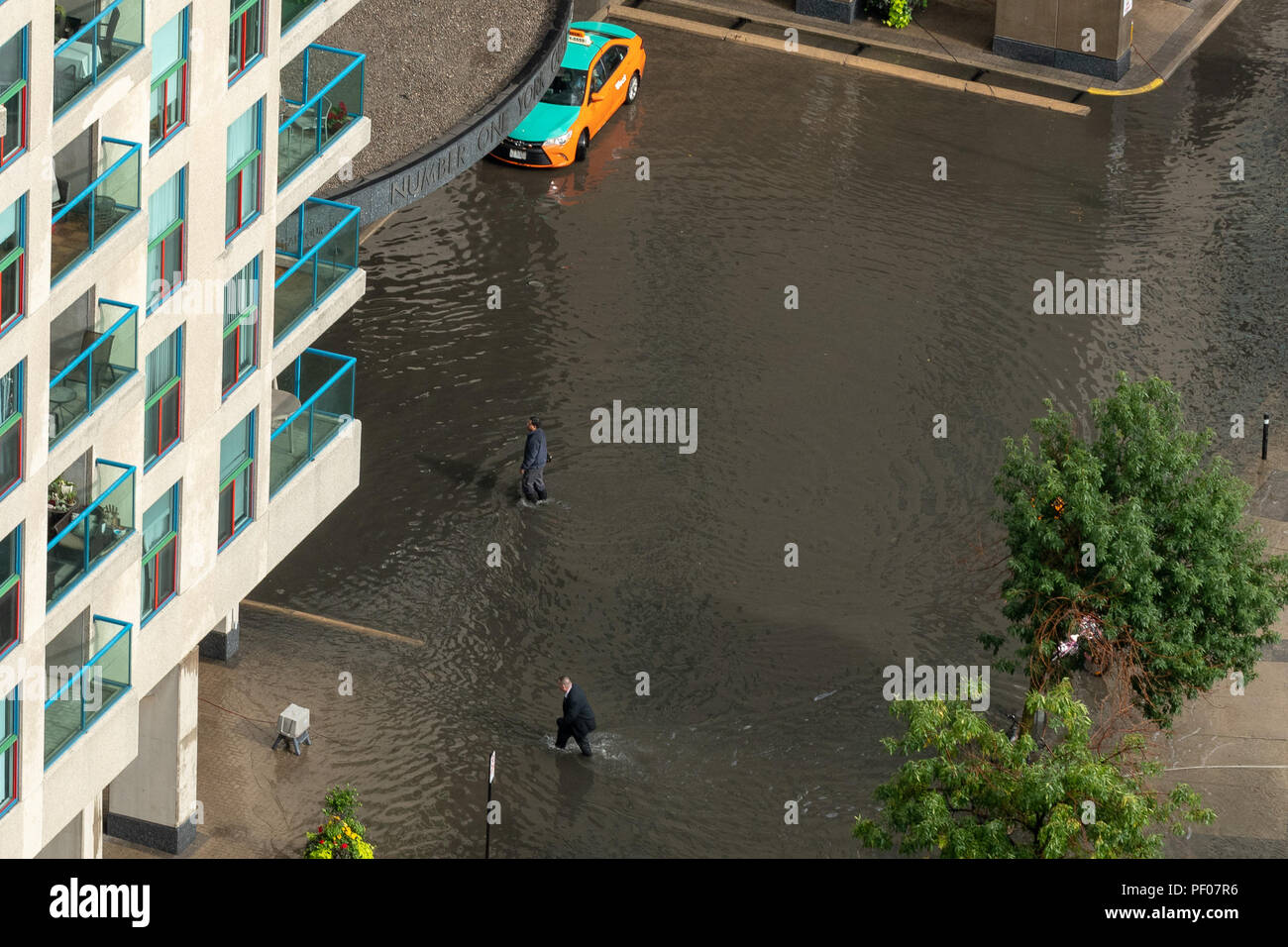 Toronto, Canada. 17th August 2018. Intense rainfall causes flash flooding in Toronto's Harbourfront area at Number One York Quay Condominium forcing residents to cross the flooded driveway in knee deep water in their business suits. Dominic Chan/EXimages Credit: EXImages/Alamy Live News Stock Photo