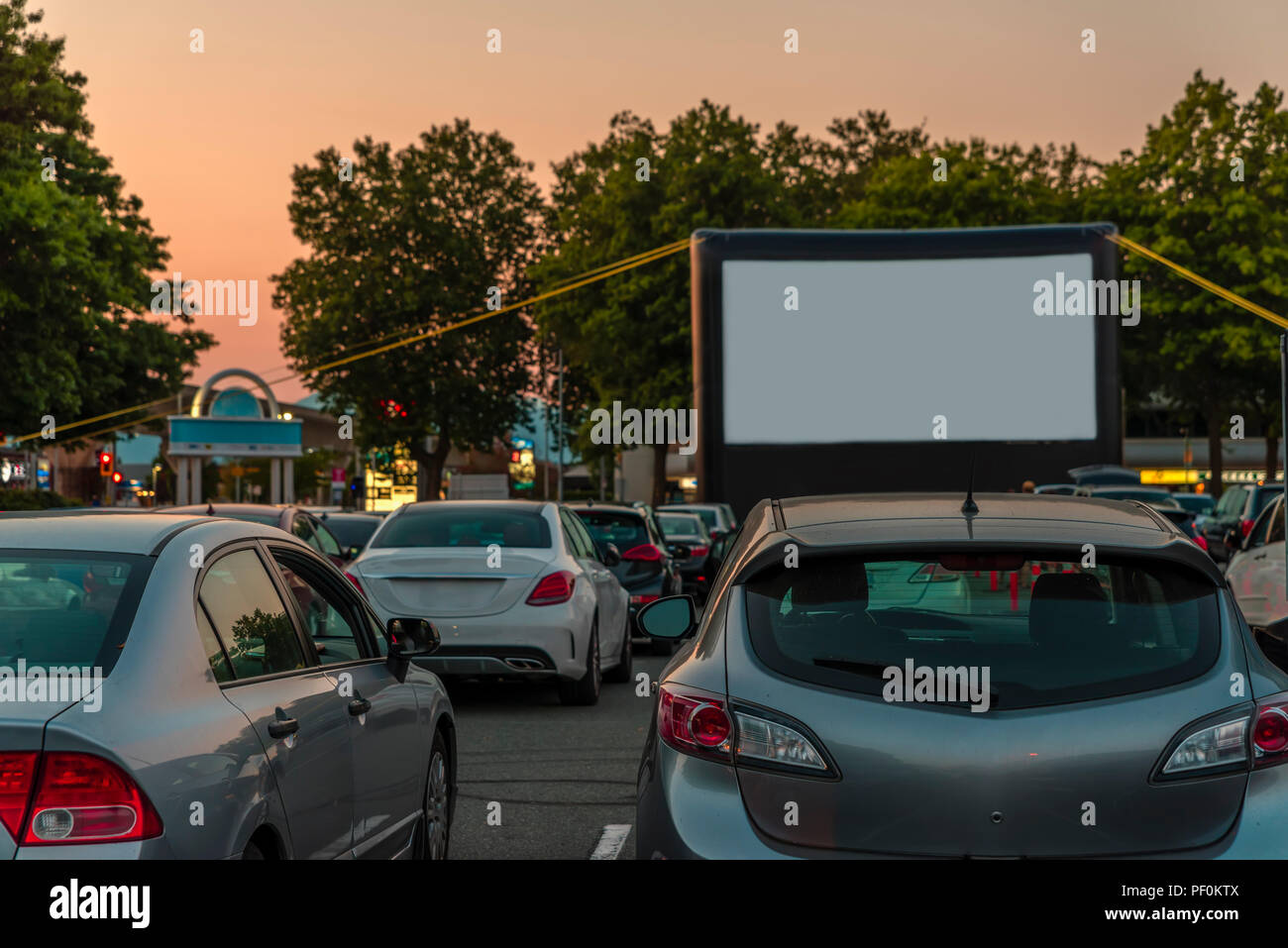 Car parking with summer cinema, green trees, cars on summer evening in modern city Stock Photo