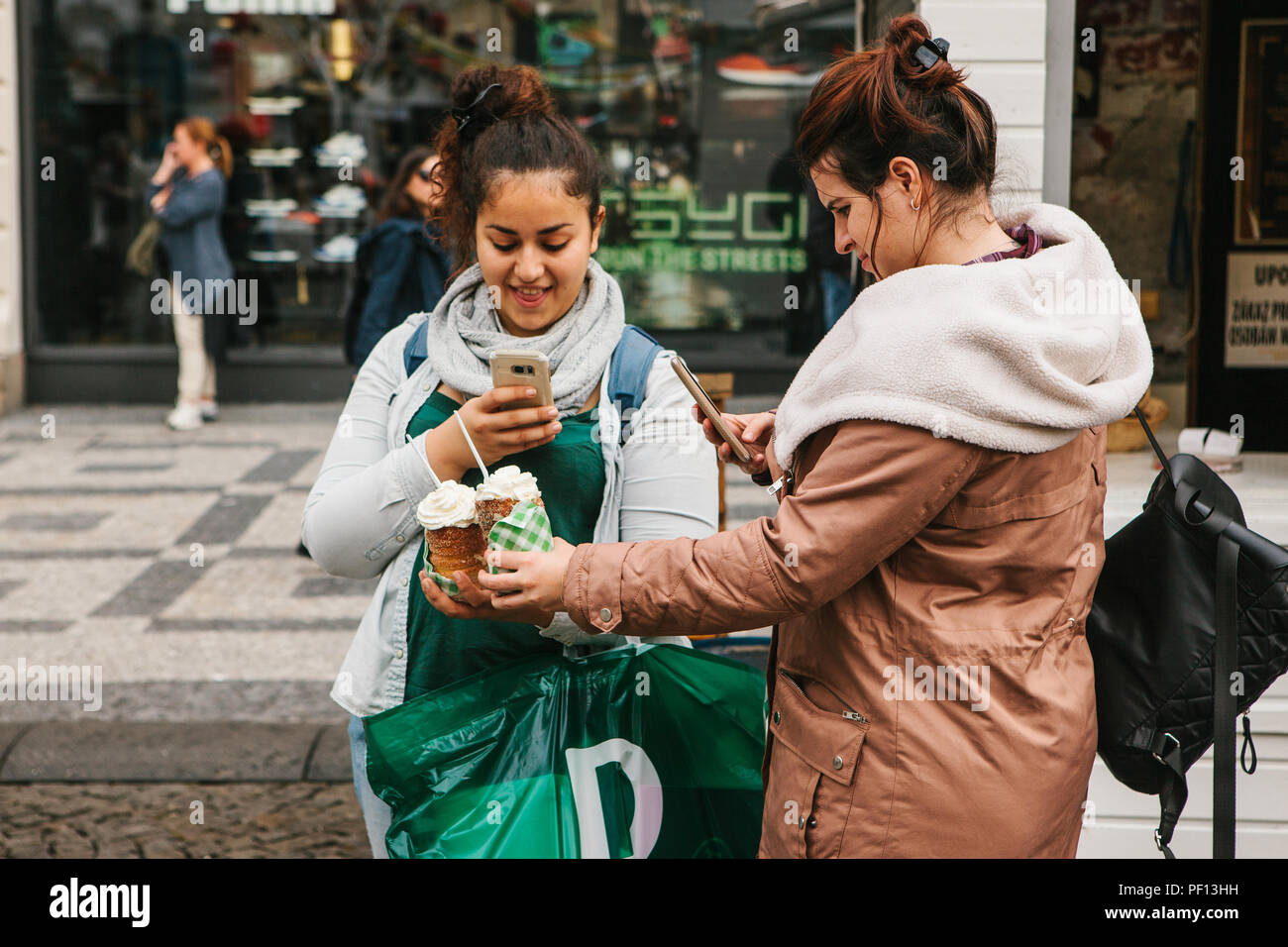 Prague, September 25, 2017: Two friends after shopping in the store stand on the street and take pictures of a traditional Czech dessert called Tridlo and make a post in social networks Stock Photo