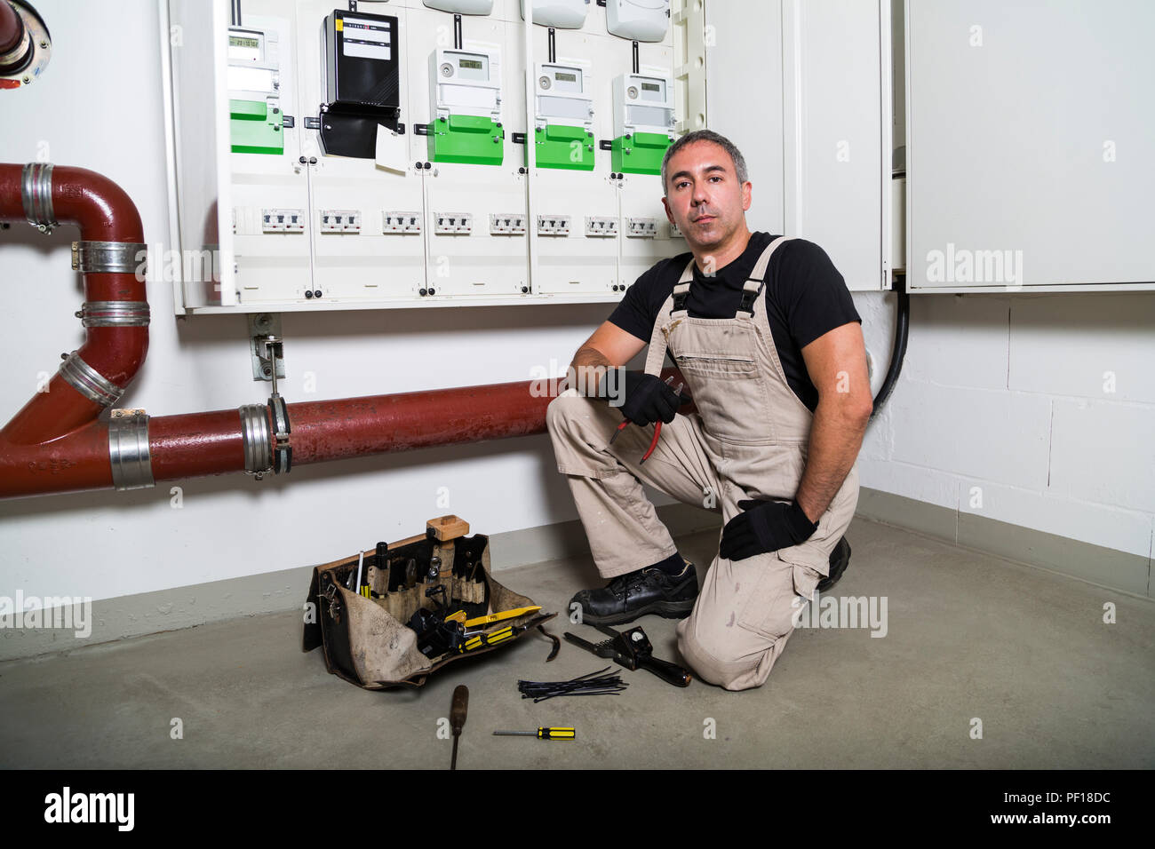 Electrician with box of tools seating near distribution or fuse board Stock Photo