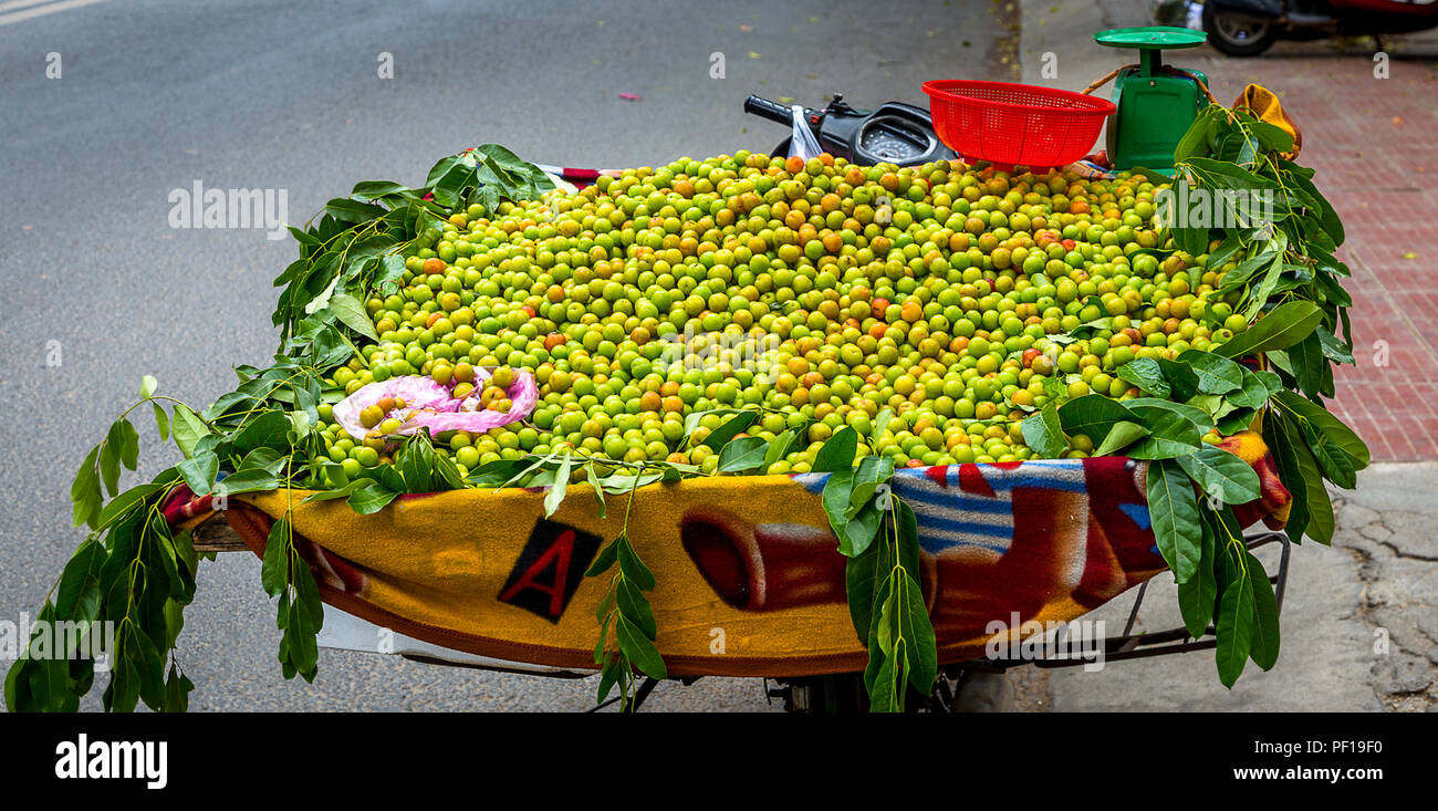 Motorcycle carries a big batch of small green round fruit for sale. Stock Photo