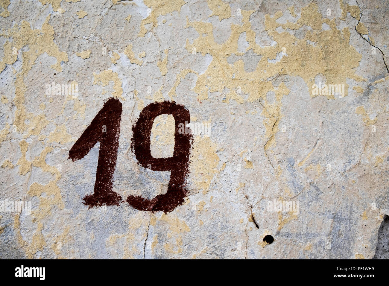Street address number 19 (nineteen) painted on a textured cement wall with cracks and peeling paint Stock Photo