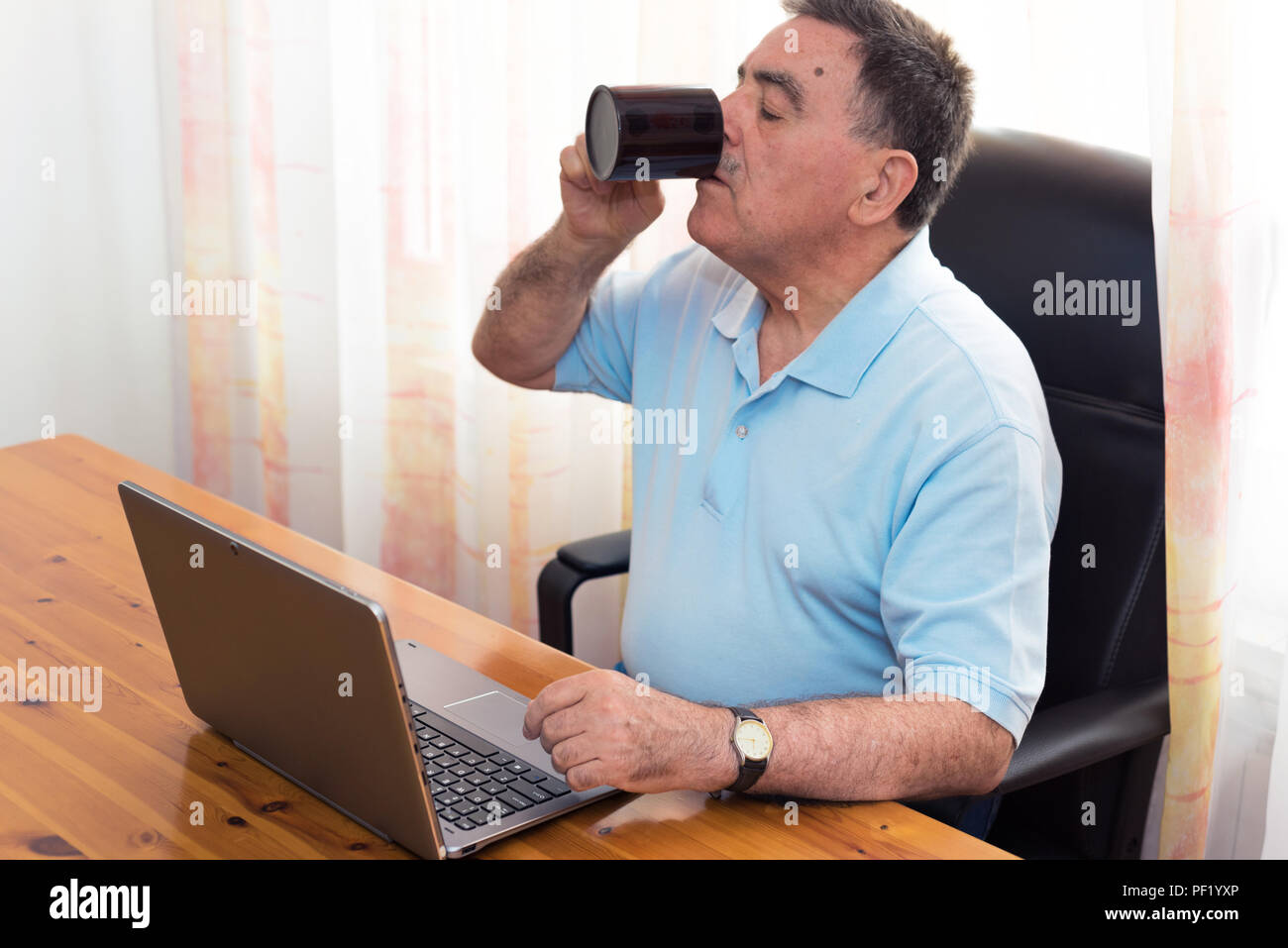 Senior man having a coffee and working on his computer Stock Photo