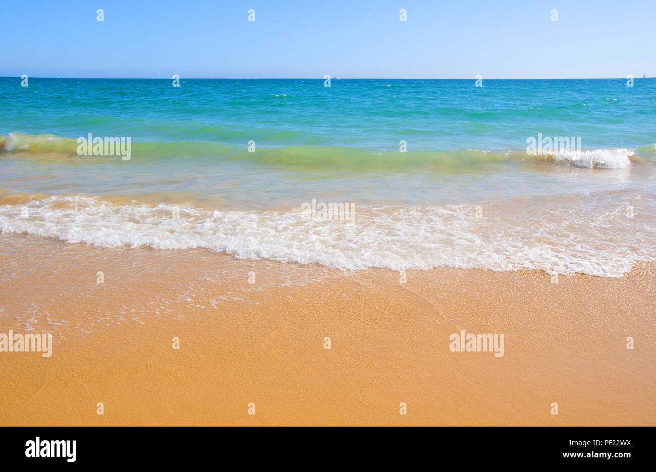 Ocean shore with yellow sand, blue water and waves, summer, Portugal Stock Photo