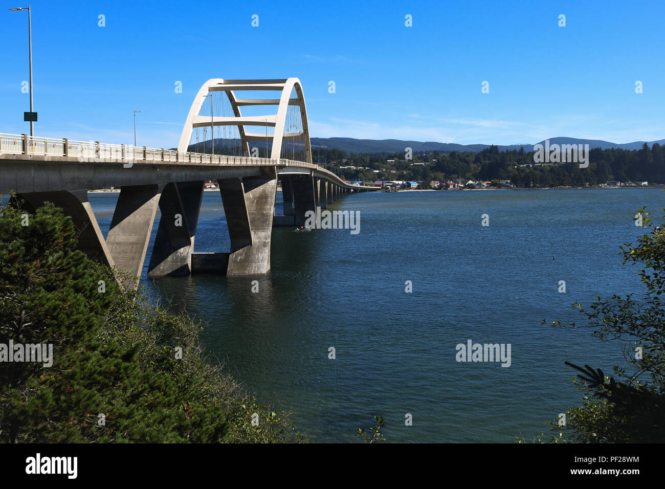 The U.S. Route 101  Alsea Bay Bridge and town of Waldport on the far side of it. A small boat passes underneath the span. Stock Photo