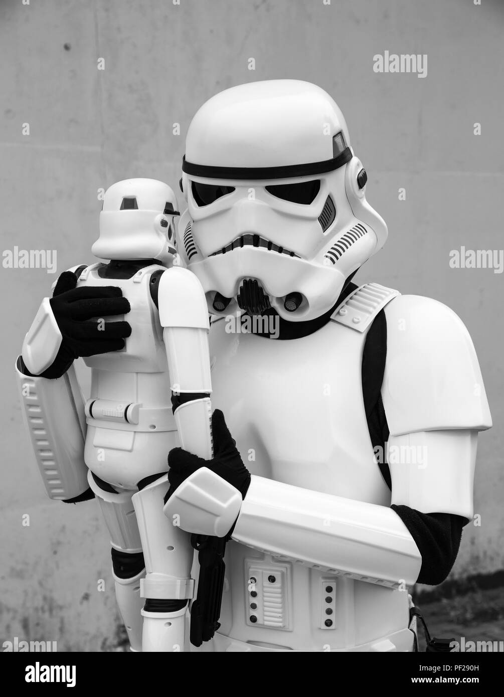 A male cosplayer dressed as a Stormtrooper from the Star Wars franchise holding a Stormtrooper toy tightly in a funny father and son lifestyle image. Stock Photo