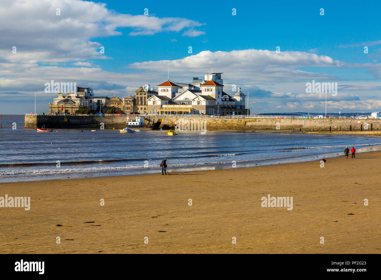 Dog walkers and a metal detectorist on the beach in front of Knightstone Island in winter at