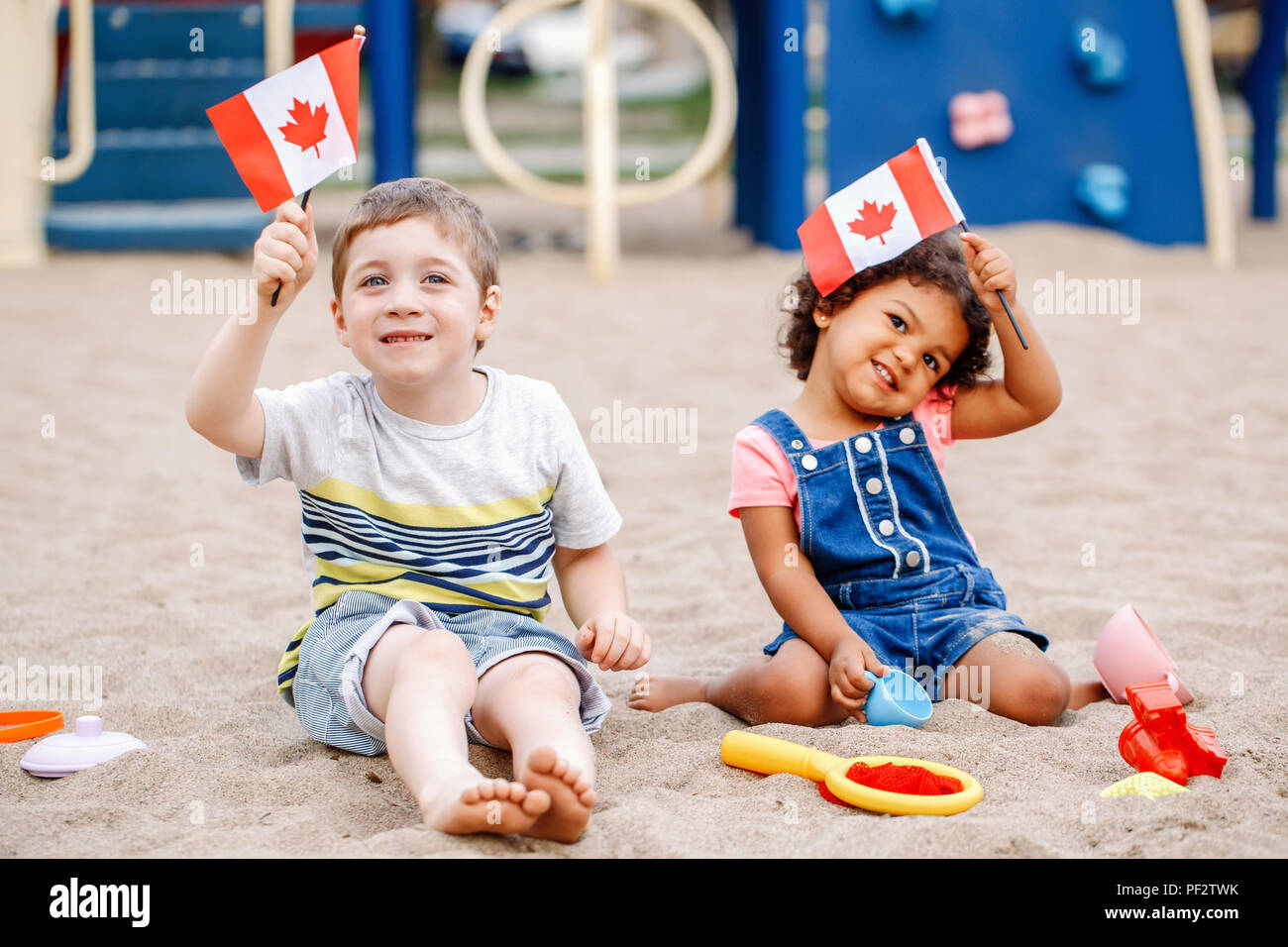 Portrait of adorable cute little Caucasian boy and latin hispanic baby girl holding waving Canadian flags. Multiracial children celebrating Canada Day Stock Photo