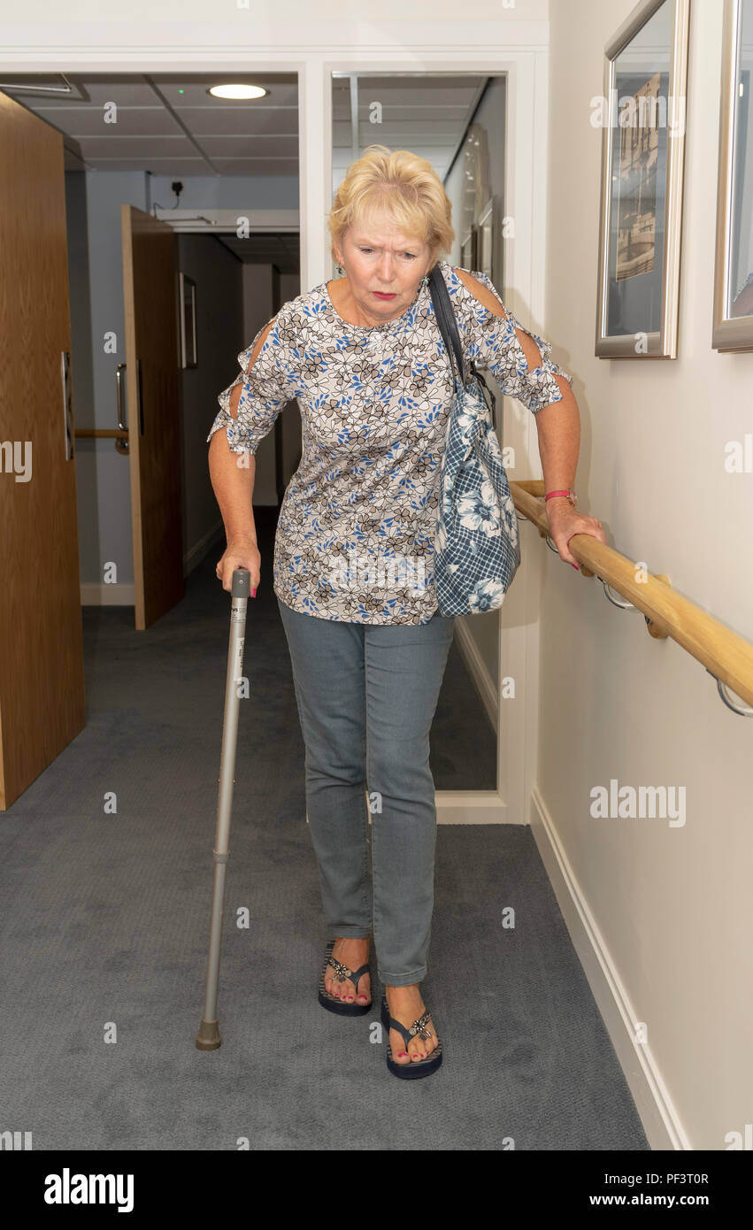 Elderly lady using a walking stick and handrail to walk in a corridor