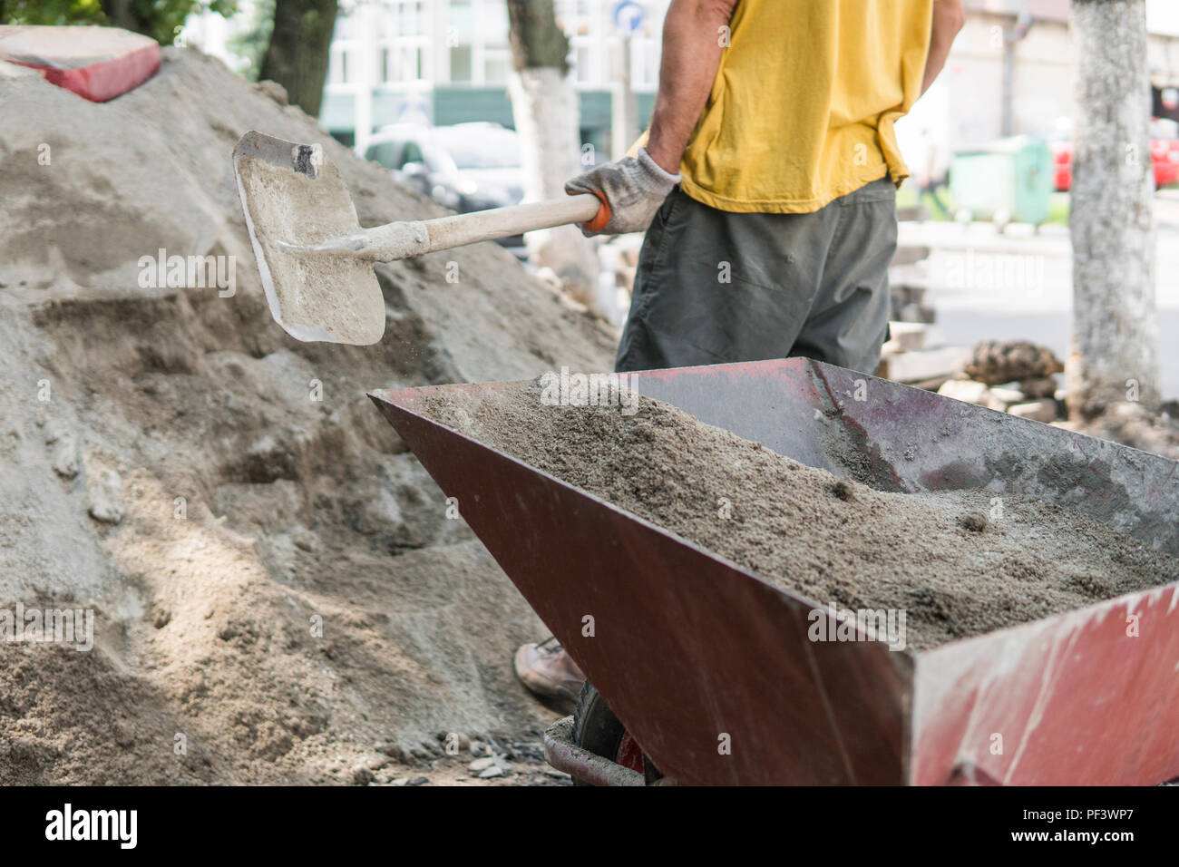 Worker use the shovel and fill the wheelbarrow with sand for construction of sidewalk road